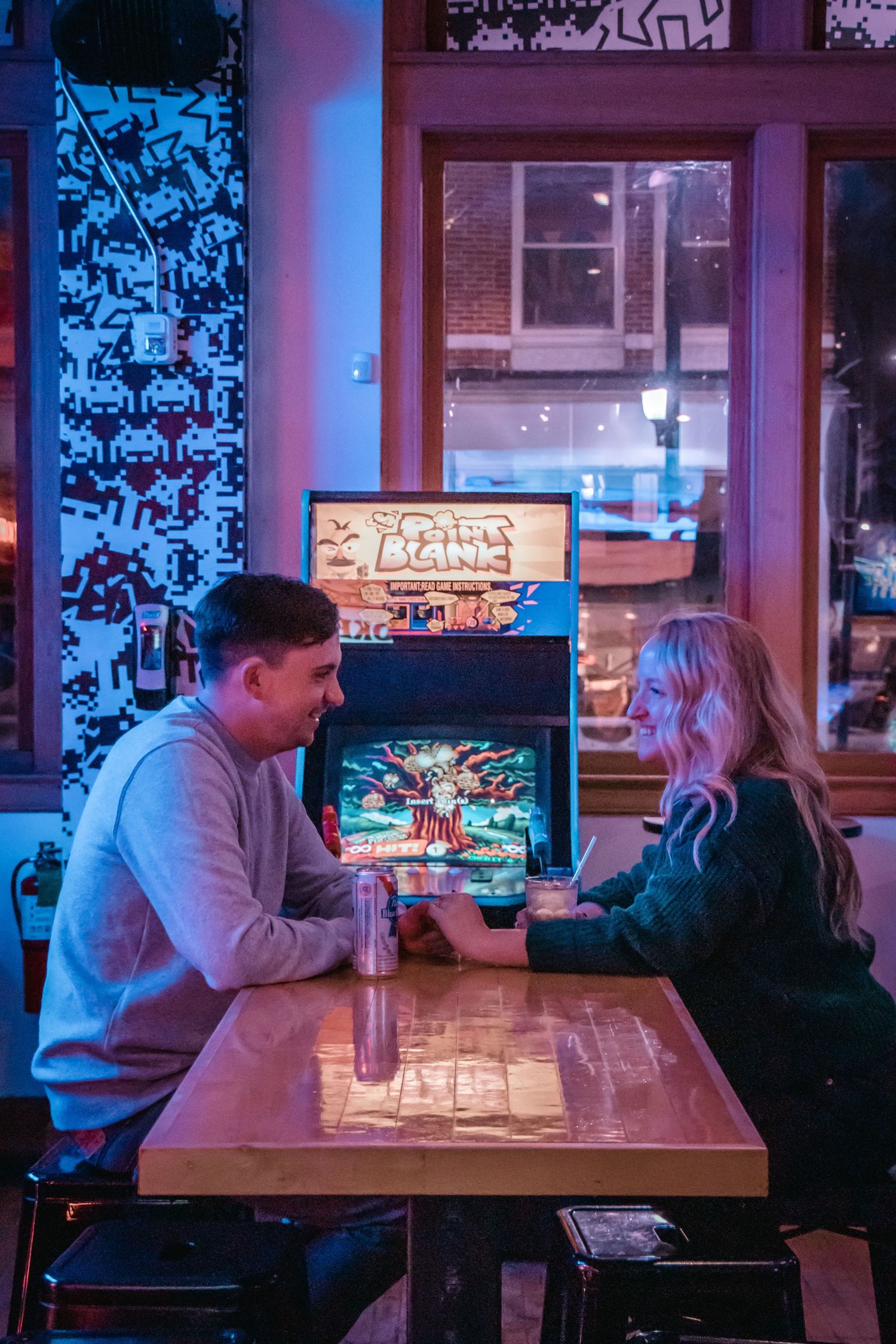 A couple plays arcade games in a neon-lit gaming cafe.