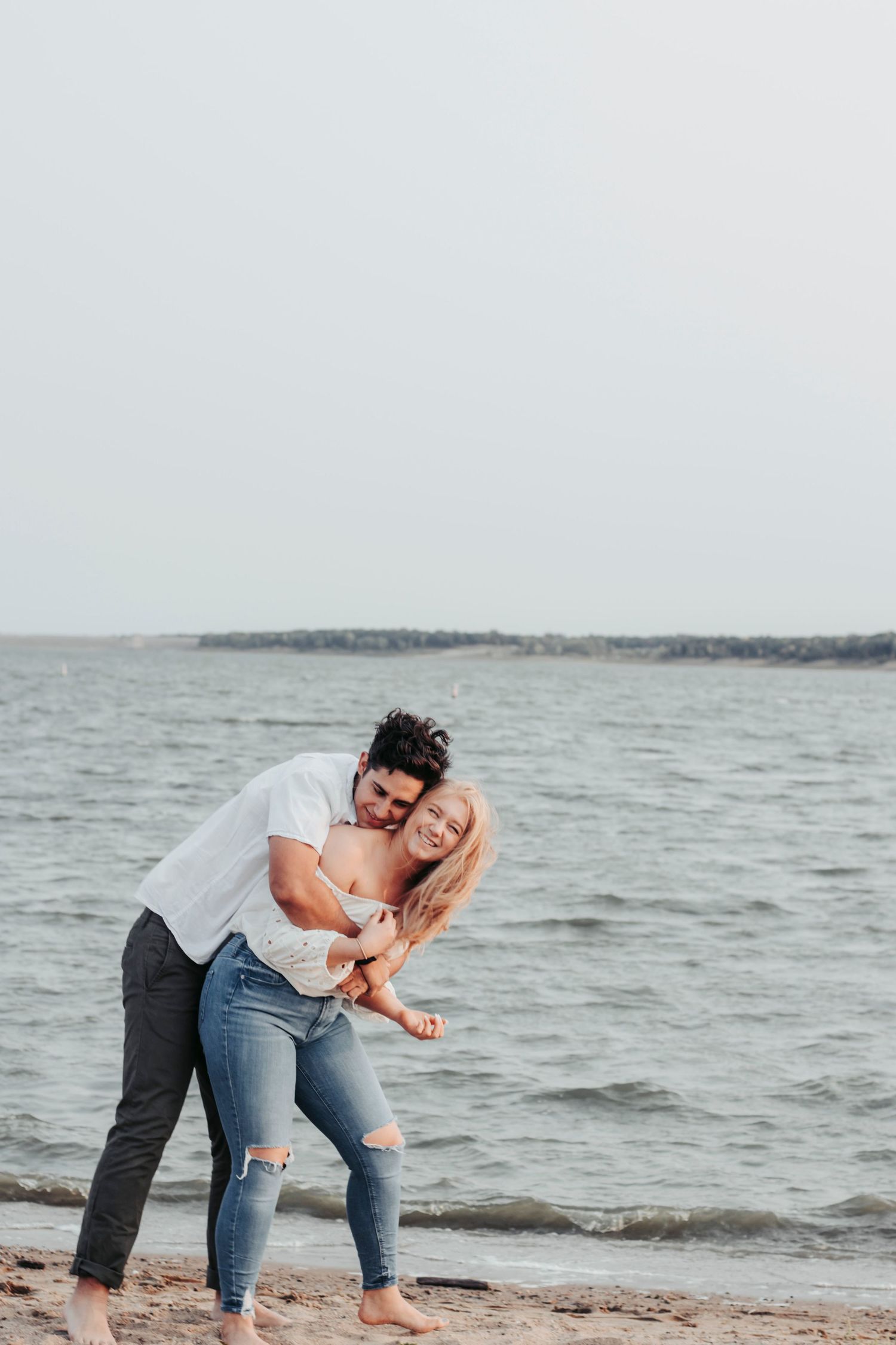 A playful couple enjoys a tender moment at the beach with waves in the background.