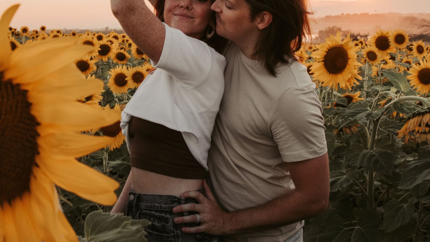 A romantic moment in a field of tall sunflowers during golden hour.