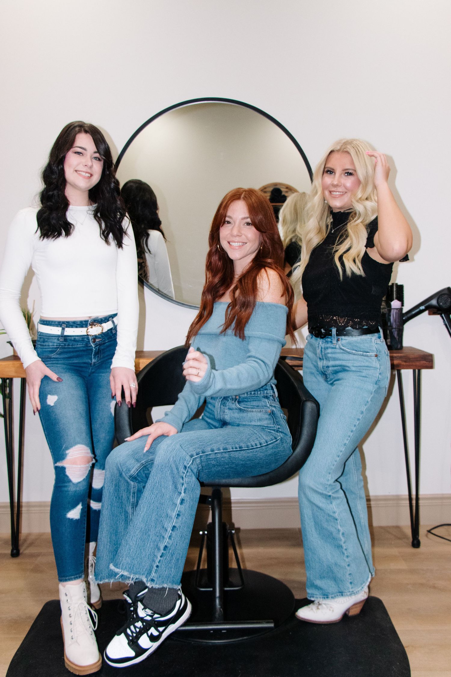 Three coworkers in denim posing together in salon setting.