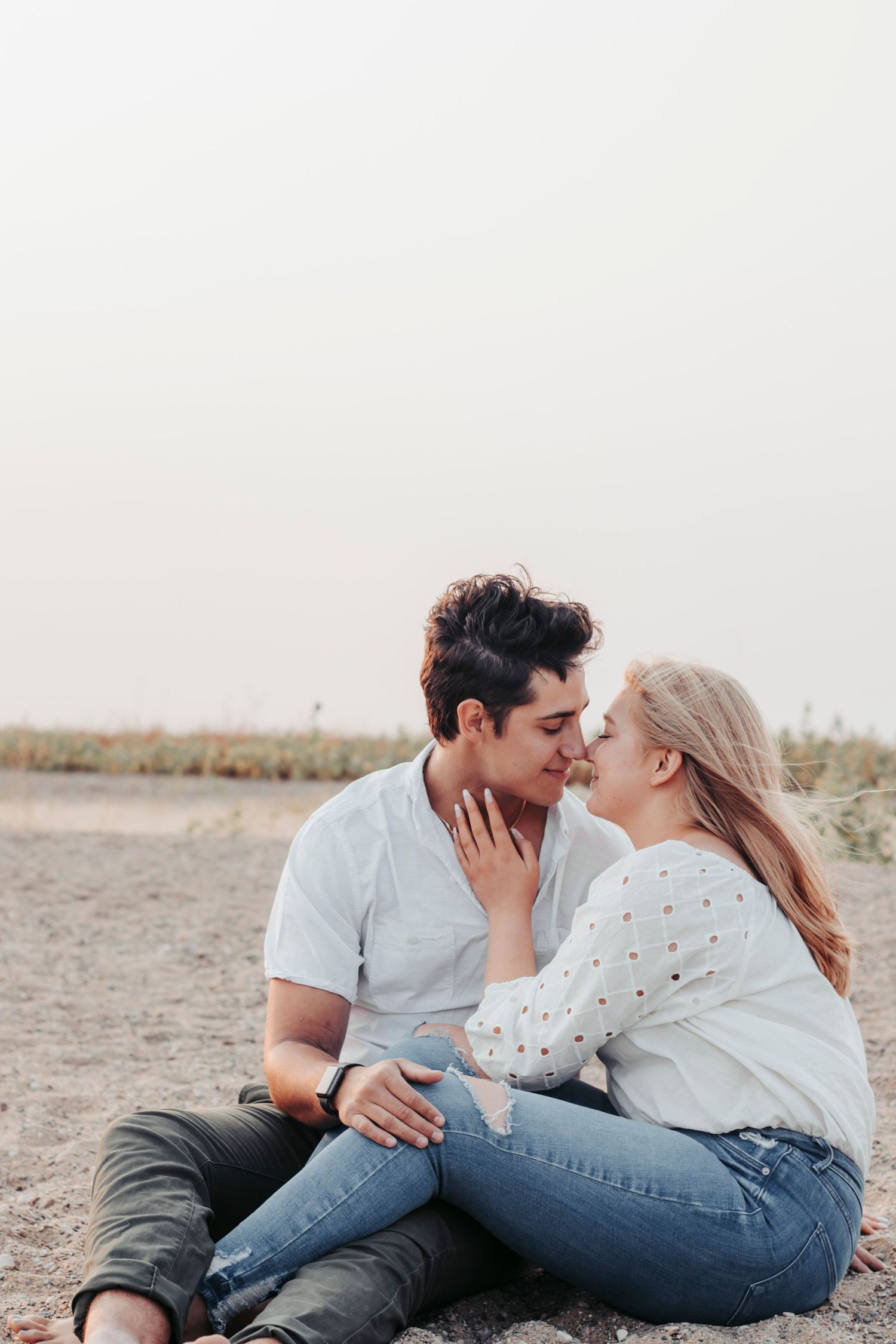 A couple sits together on the beach sand sharing a tender moment.