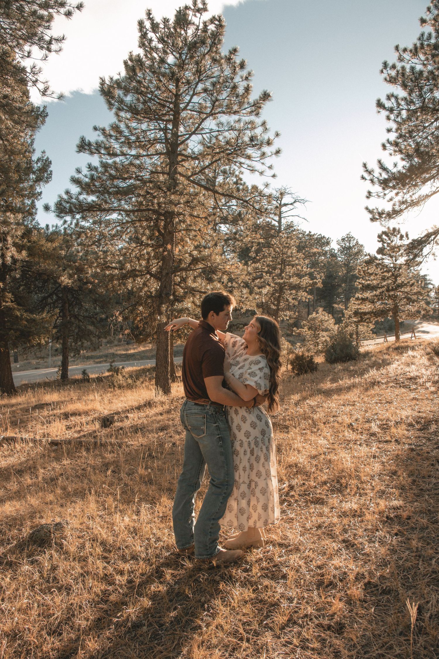 Couple sharing intimate moment among pine trees on golden hillside.