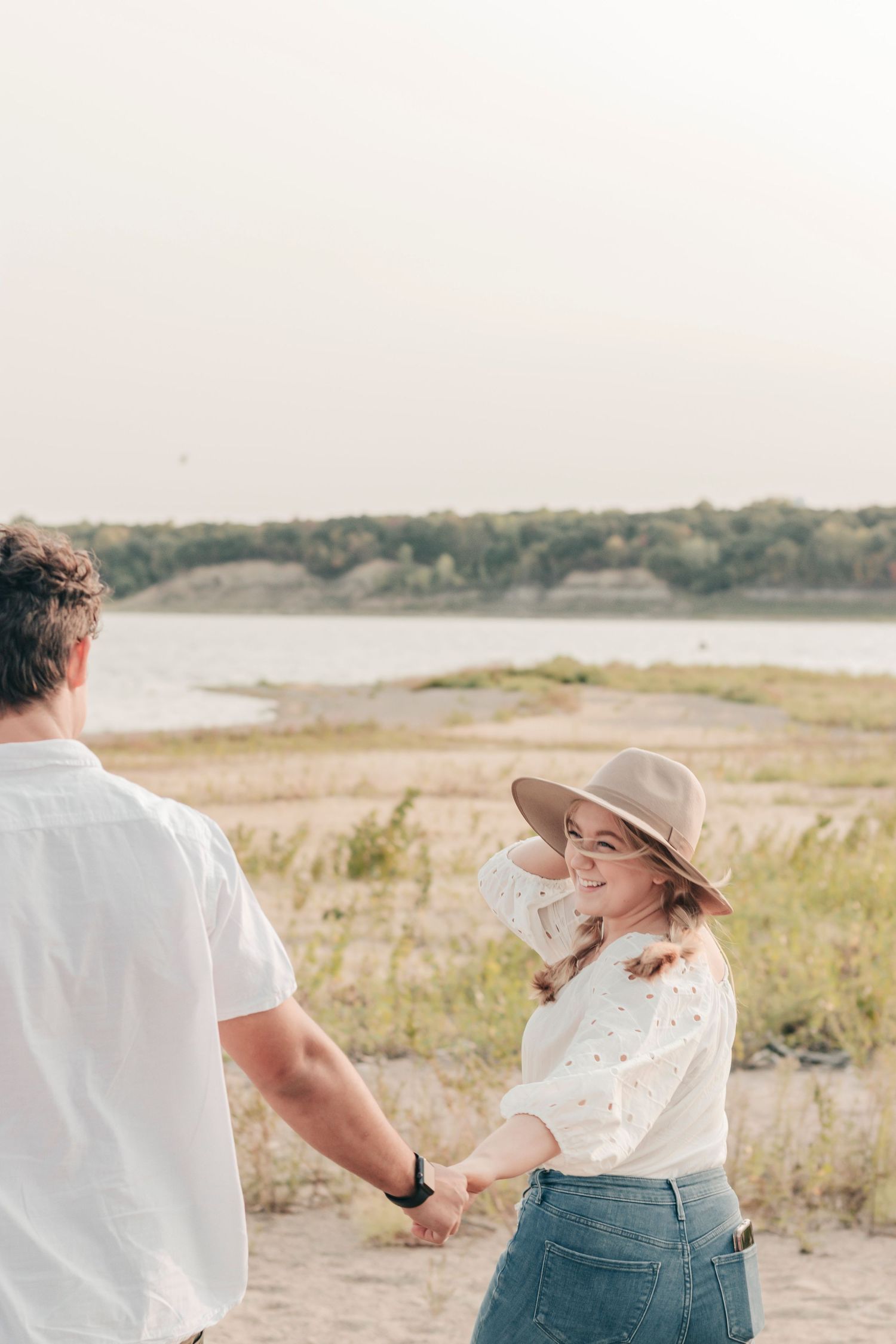 A couple holds hands while enjoying a scenic lakeside view on a sunny day.