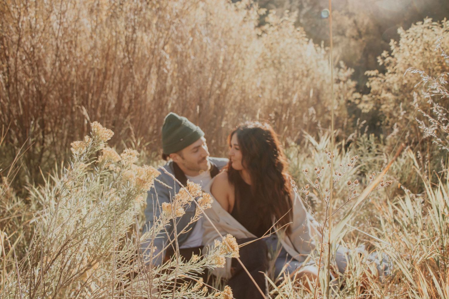 A tender moment between two people sitting in tall golden grass at sunset.