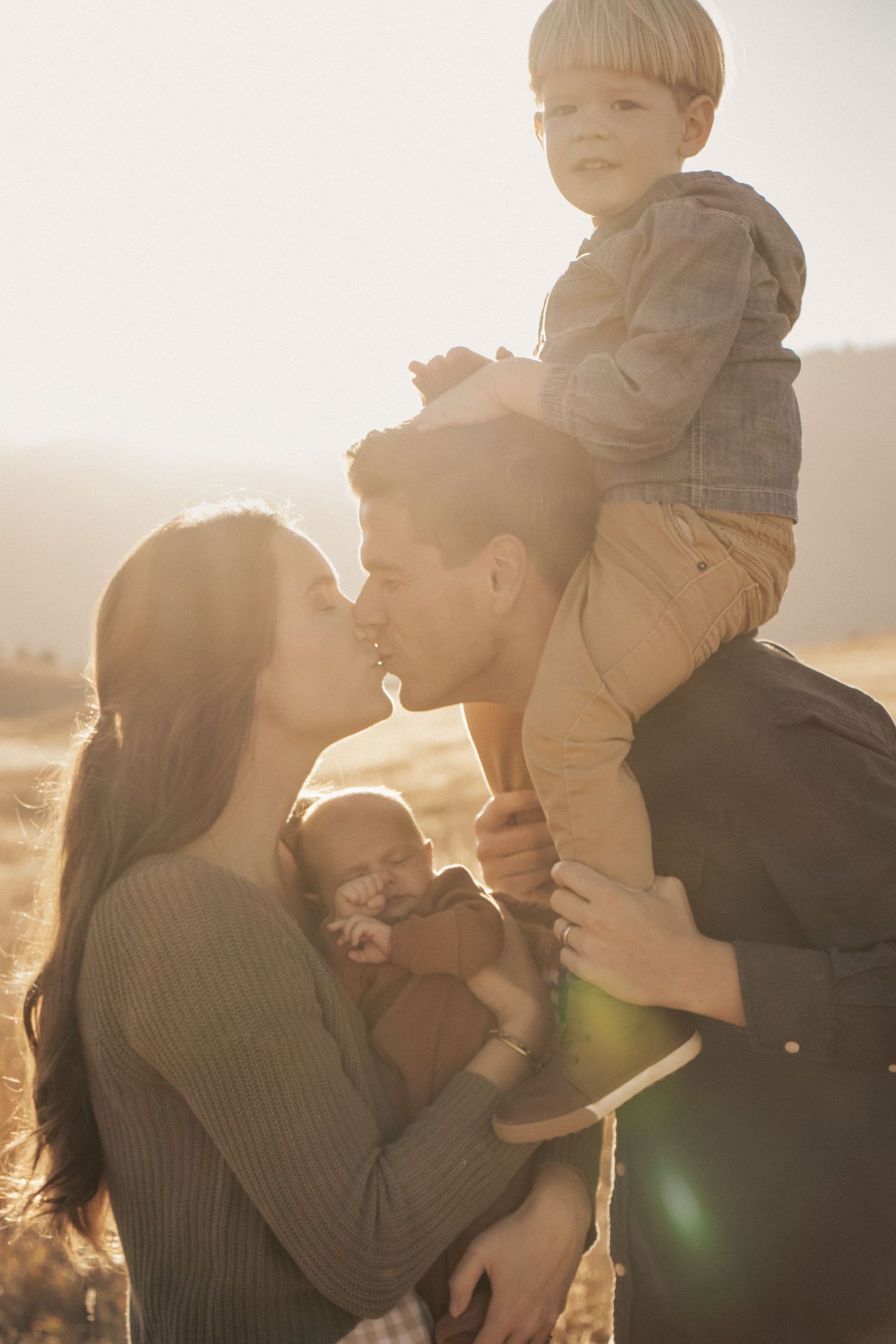 Family shares intimate moment in golden field during sunset photoshoot.