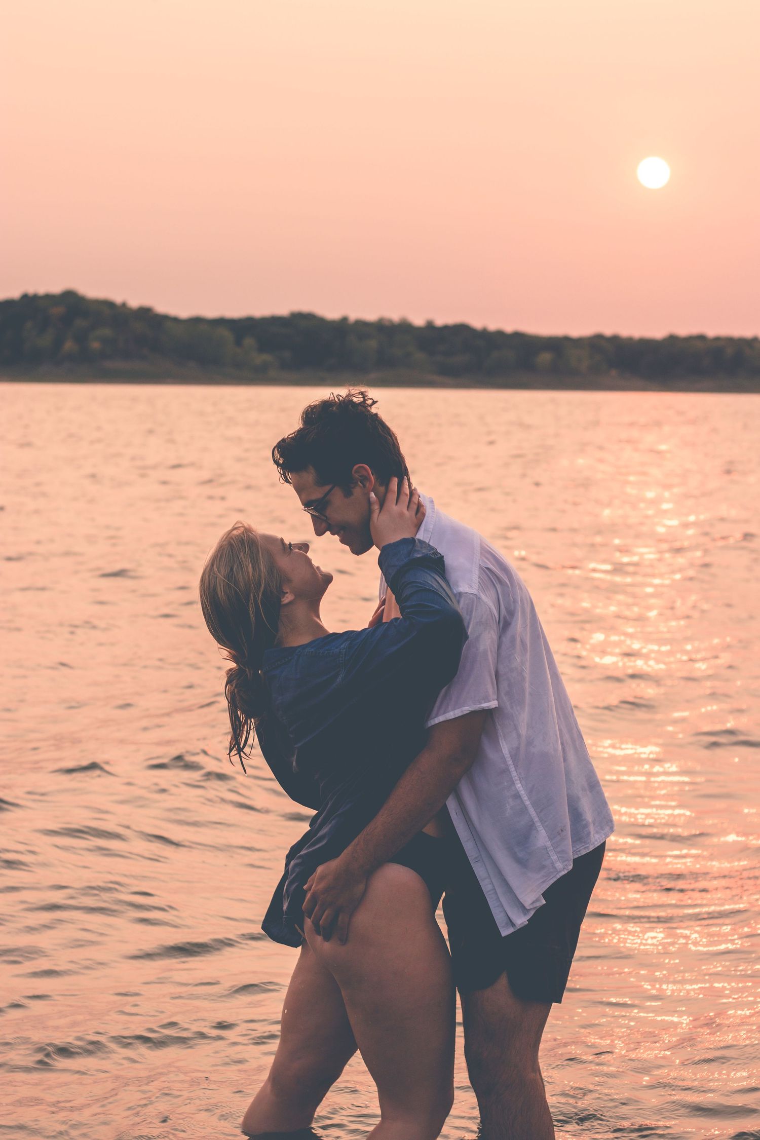 A romantic couple poses in the water during a pink sunset at the beach.