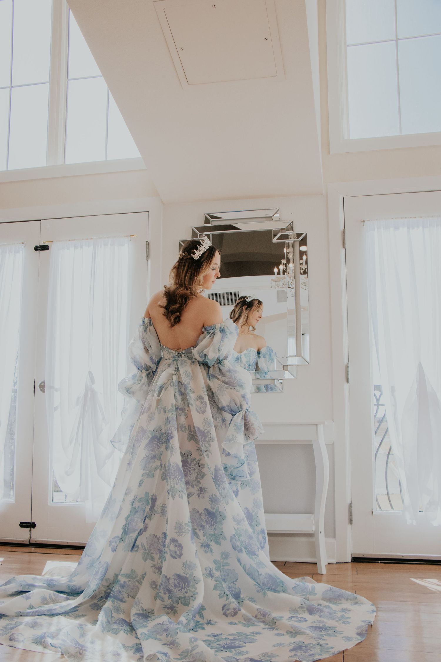 A flowing blue floral dress with a long train photographed in a bright white room with mirrors.