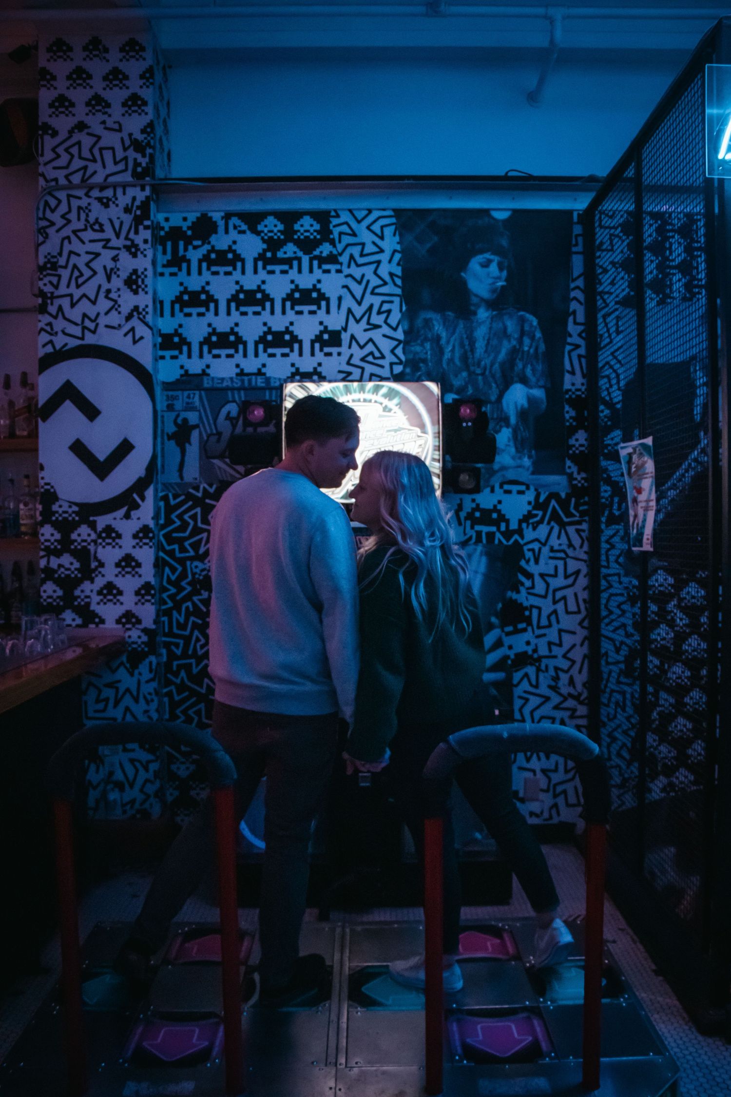 Couple sharing intimate moment in neon-lit arcade room with retro gaming posters.