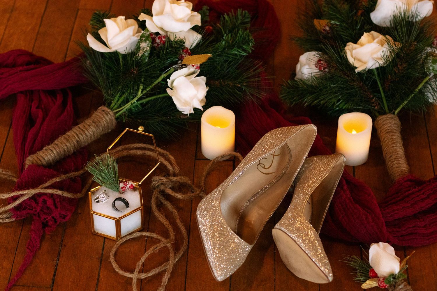 Wedding details featuring roses, evergreen sprigs, and glittery shoes in warm candlelight.