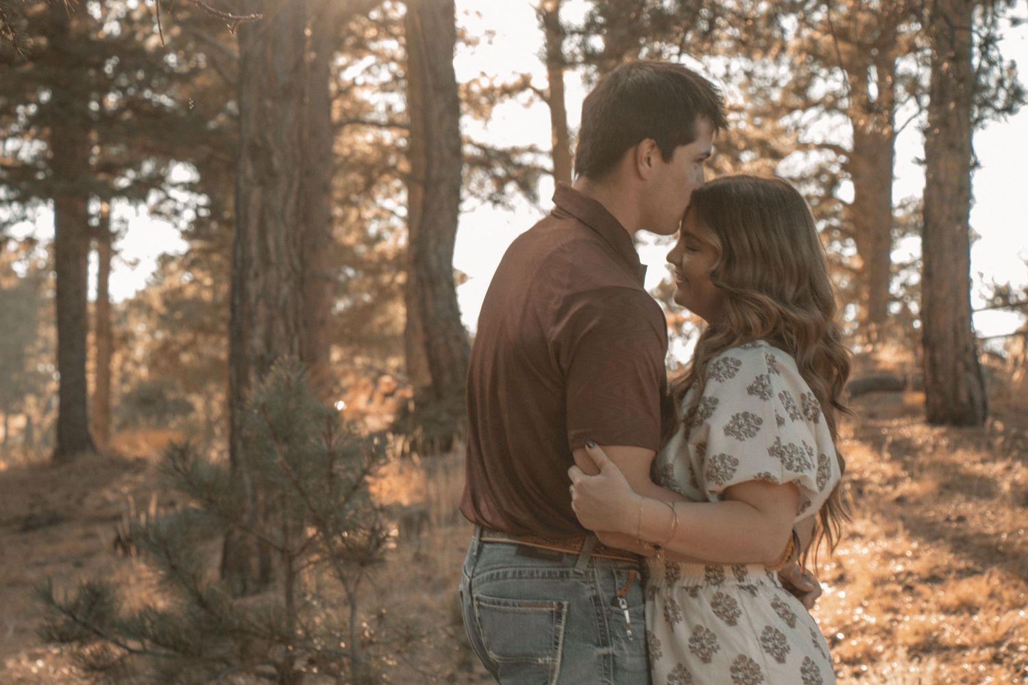 Romantic moment between couple surrounded by pine trees at sunset.