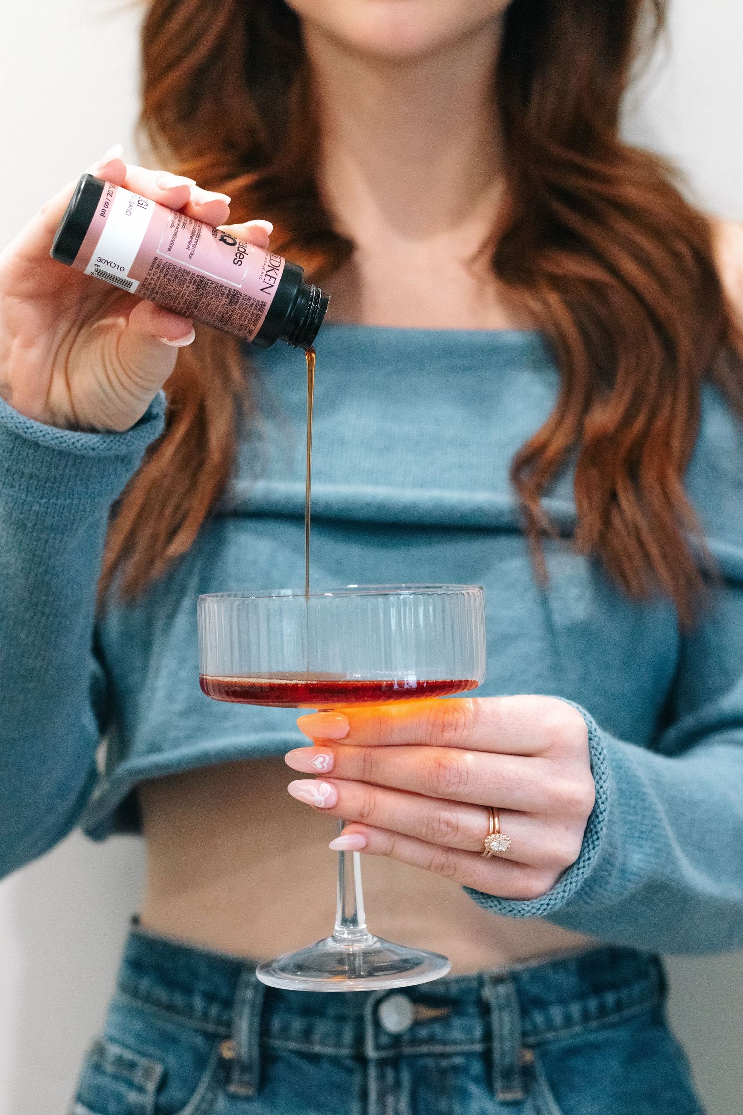 Hands pouring redken liquid from toner bottle into cocktail glass.