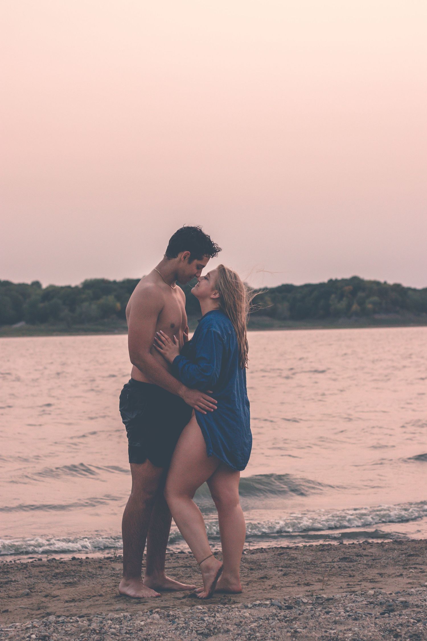 Romantic couple embracing on beach at sunset in warm lighting.