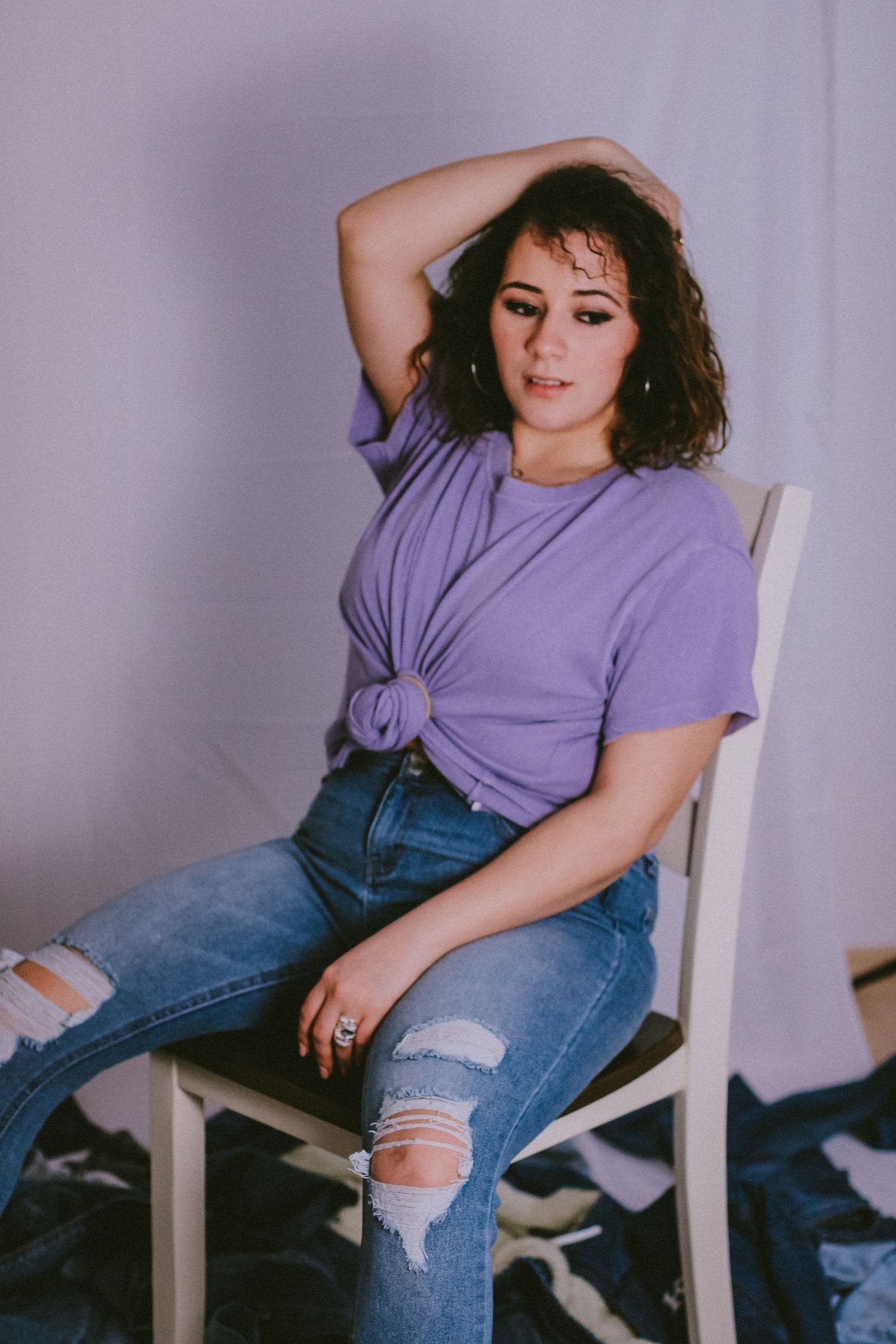 Casual portrait with purple knotted t-shirt and distressed jeans against lilac background.