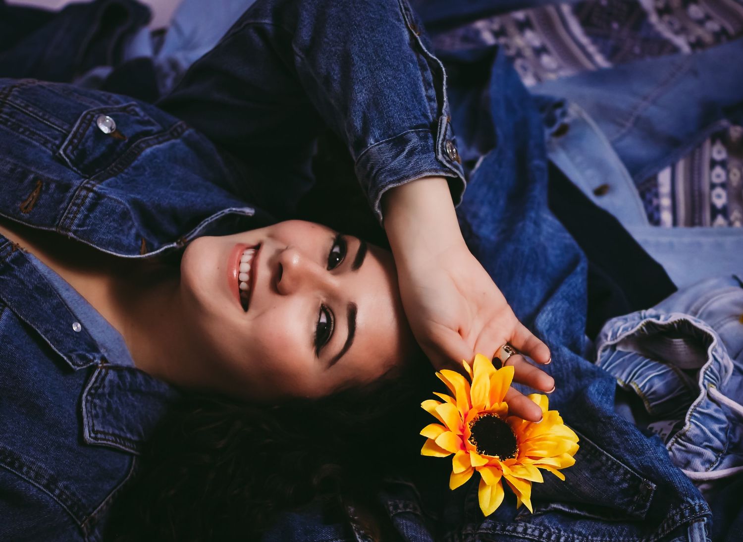 Fashion portrait with sunflower accent and denim styling against dark background.