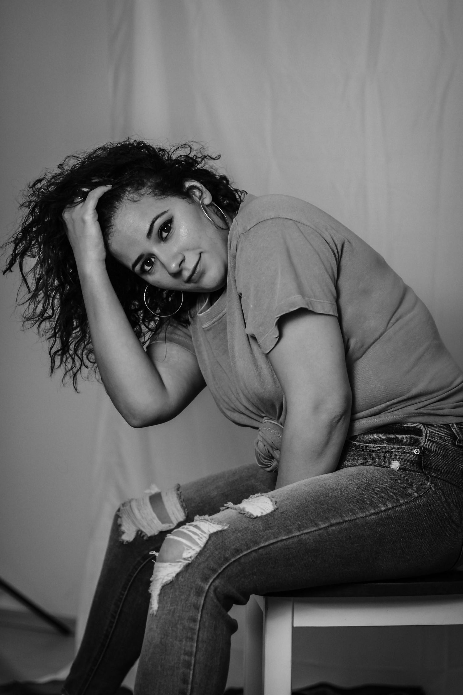 Black and white portrait showing relaxed pose on white chair with textured styling.