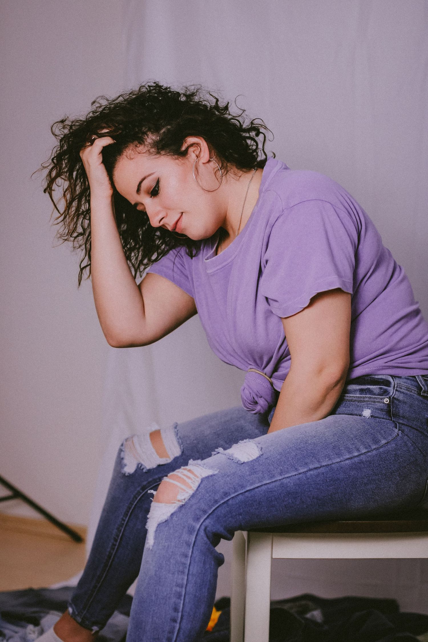 Artistic portrait in purple t-shirt showing relaxed pose against lavender backdrop.