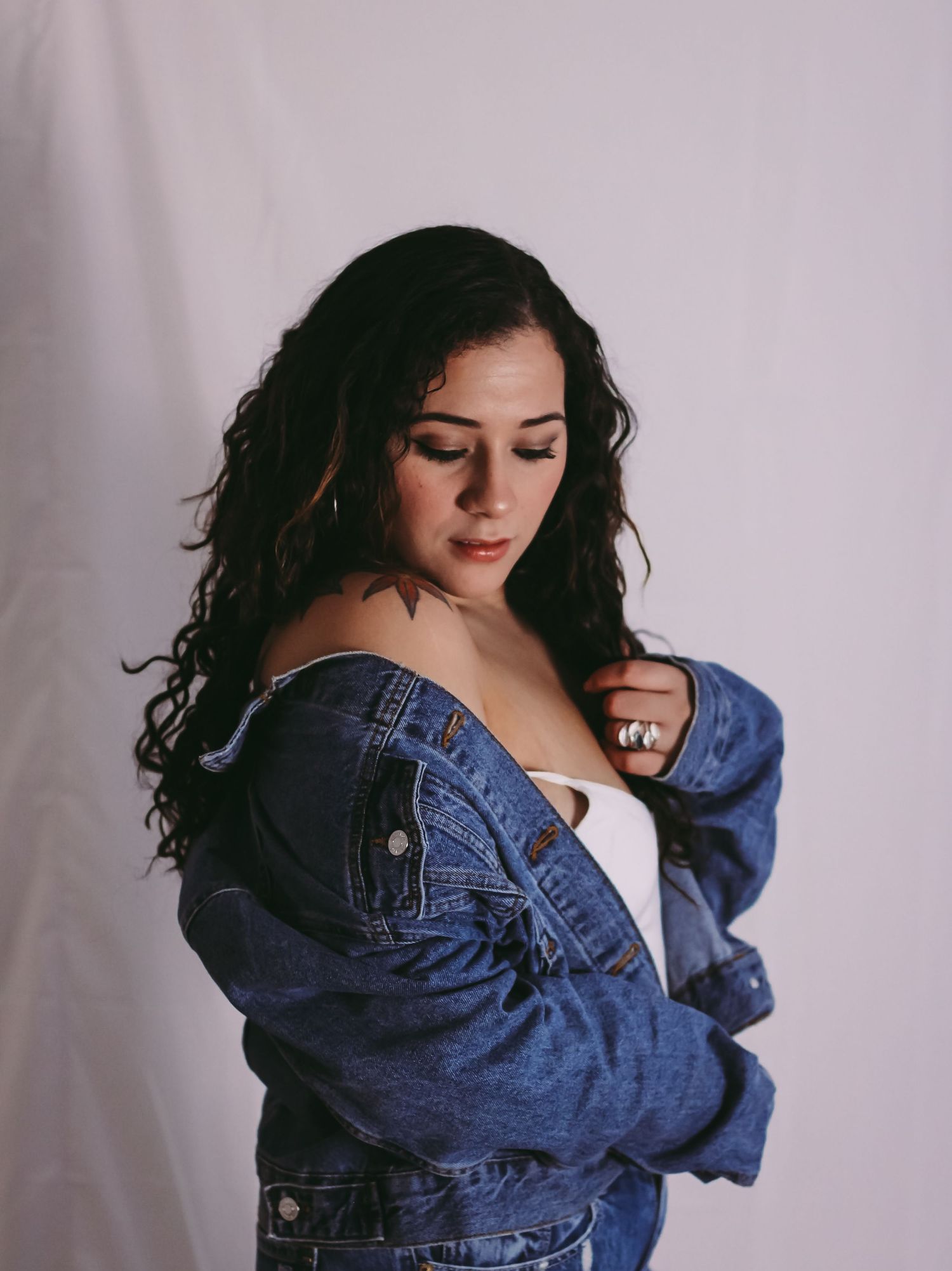 Moody fashion portrait featuring denim jacket and natural curls against light backdrop.