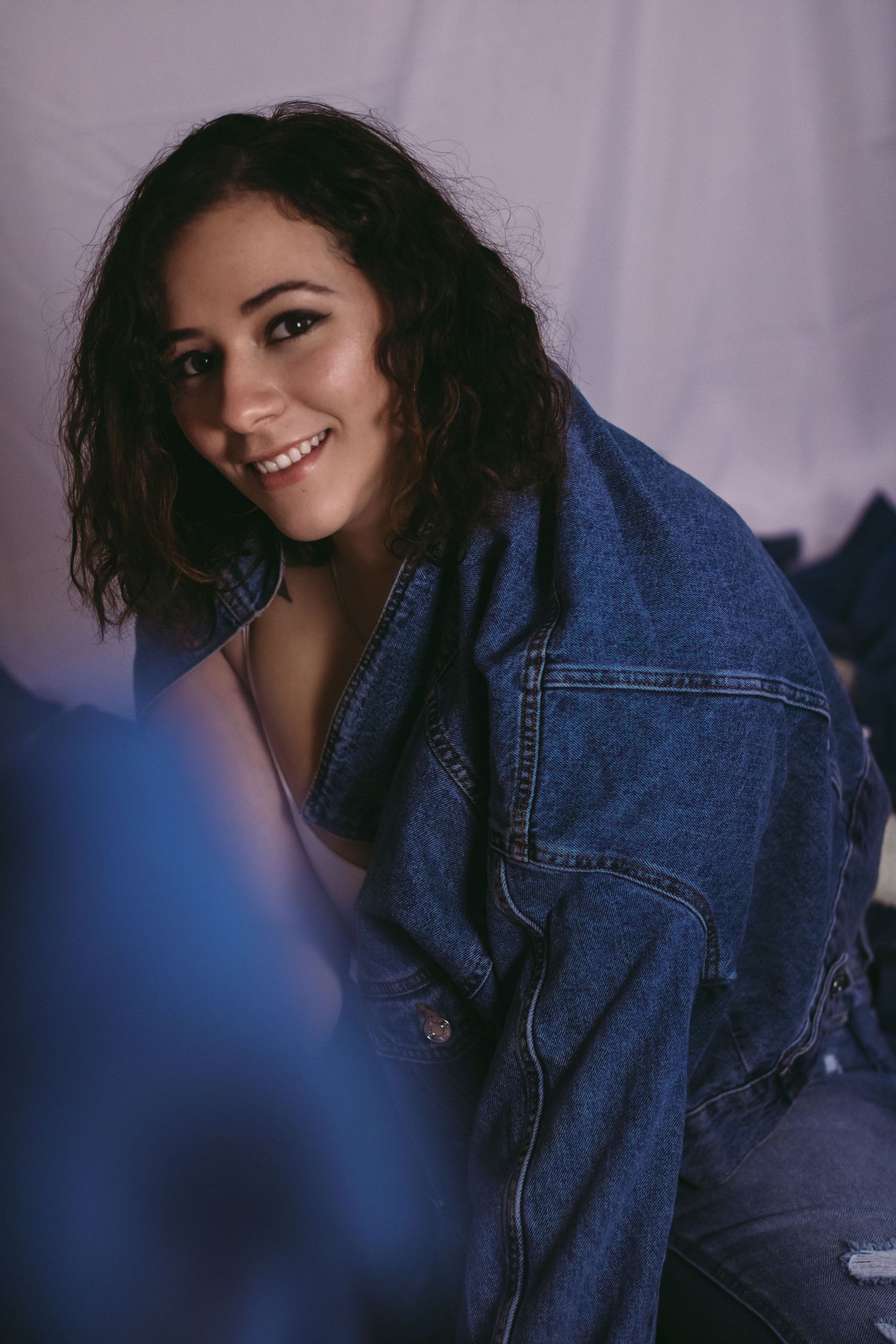 Candid fashion portrait featuring oversized denim jacket against purple backdrop.