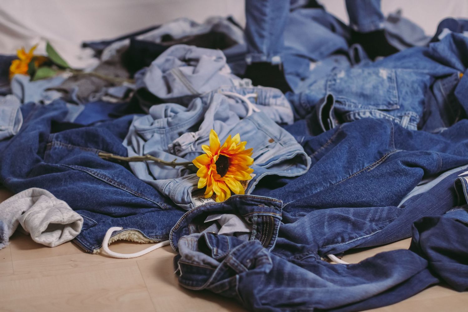 Scattered denim garments with bright sunflower create artistic still life composition.