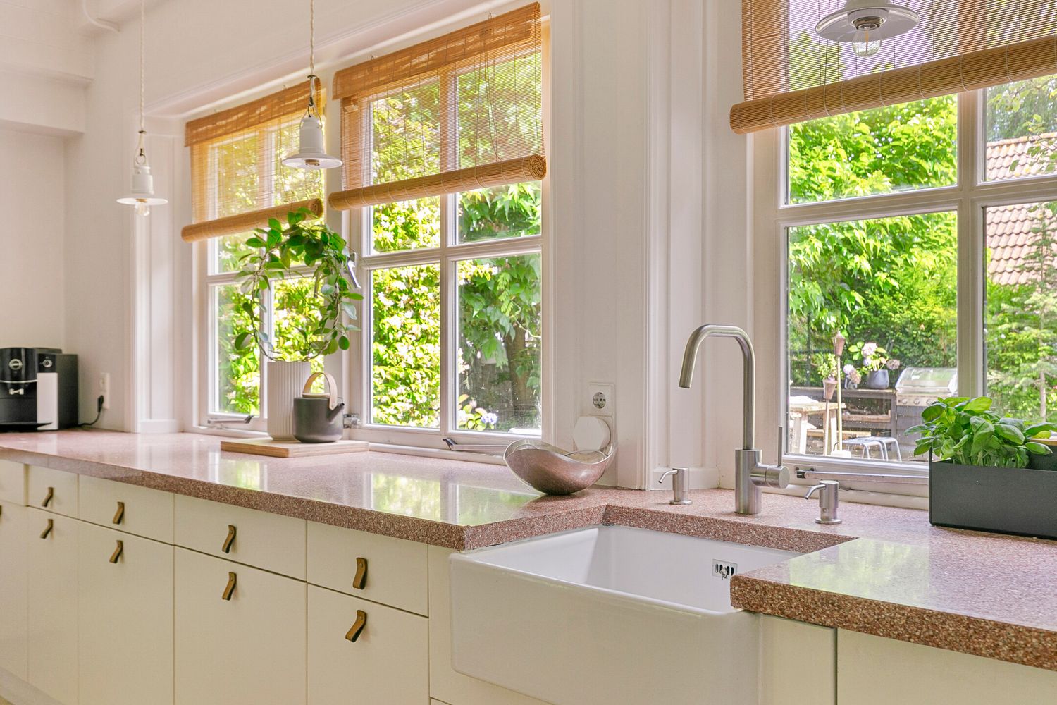 Sunny kitchen counter with farmhouse sink and windows overlooking green garden view.