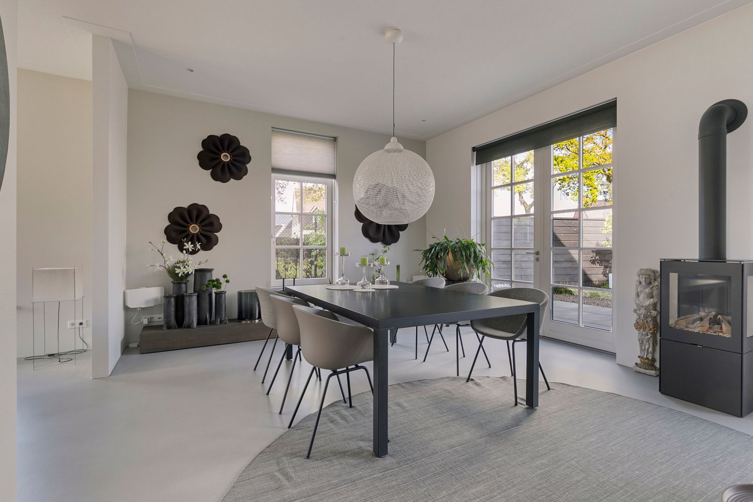 Elegant dining space with gray chairs, black table, and decorative flower wall art featuring a wood-burning stove.