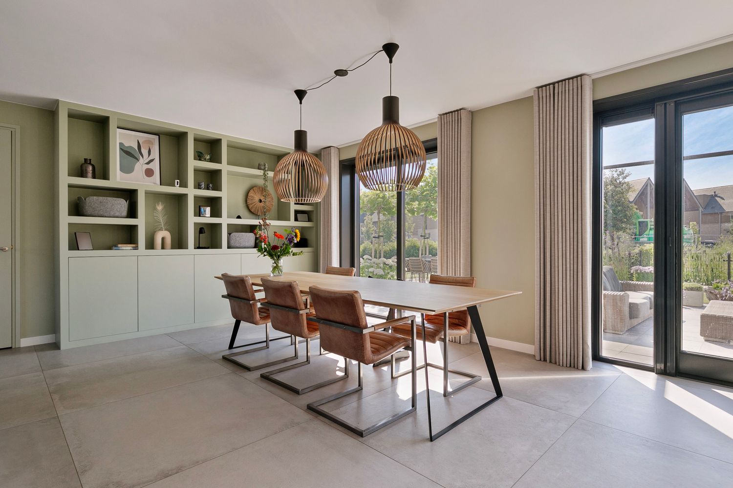 Contemporary dining room with built-in shelving, wooden table, and leather chairs beneath designer pendant lights.