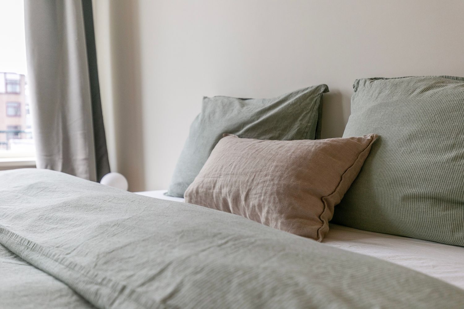Close-up of bed with soft gray and beige linen pillows and duvet cover.