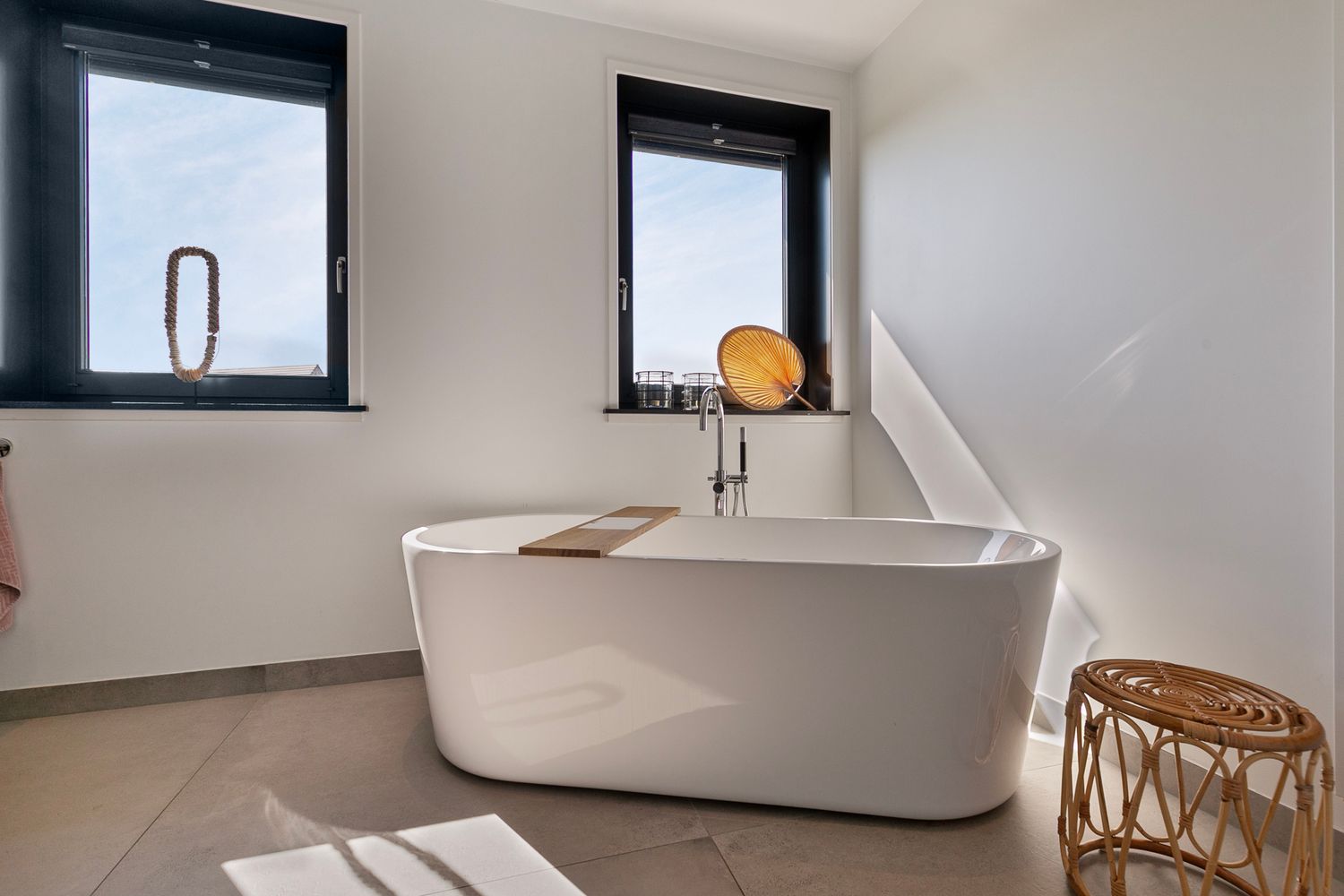 Sleek freestanding white bathtub in minimalist bathroom with black-framed windows.