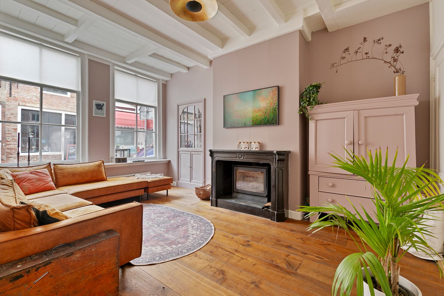 Cozy living room with leather sofa, fireplace, wooden floors and high ceilings with large windows.