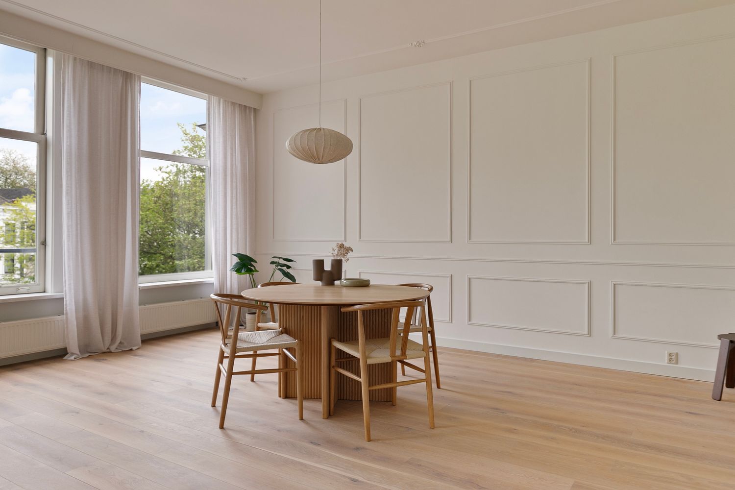 Elegant dining room with round wooden table, woven pendant light, and classic wall moldings.
