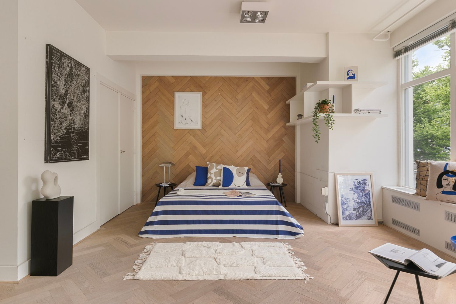 Minimalist bedroom featuring herringbone wood wall, striped bedding, and white shelving.