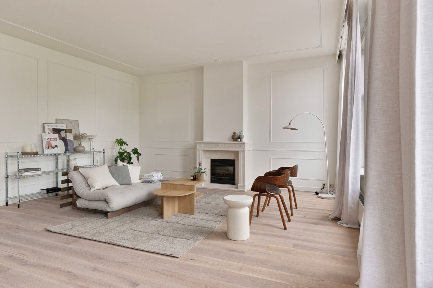 Modern minimalist living room with white chaise lounge, wooden chair, and fireplace in bright space with light wood floors.