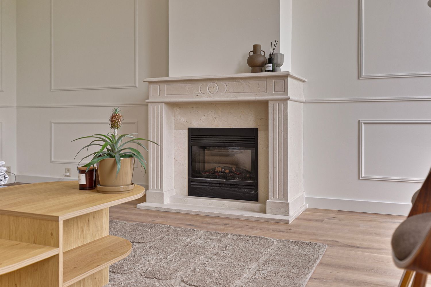 Cozy living space with marble fireplace, wood floors, and built-in wall paneling.
