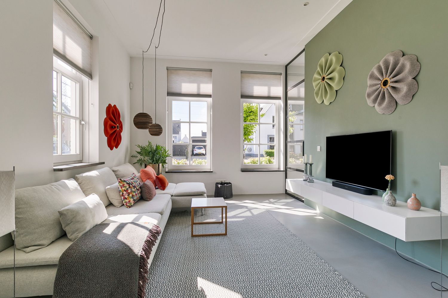 Bright living room with gray sectional sofa, floral wall decor, and mint accent wall featuring mounted TV.