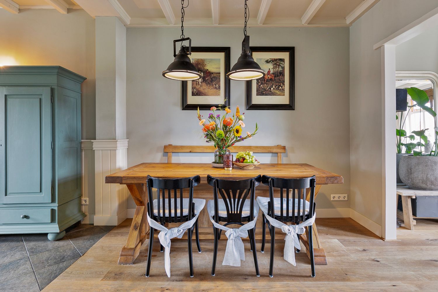 Rustic dining room featuring wooden table with black chairs under pendant lights and coastal decor.