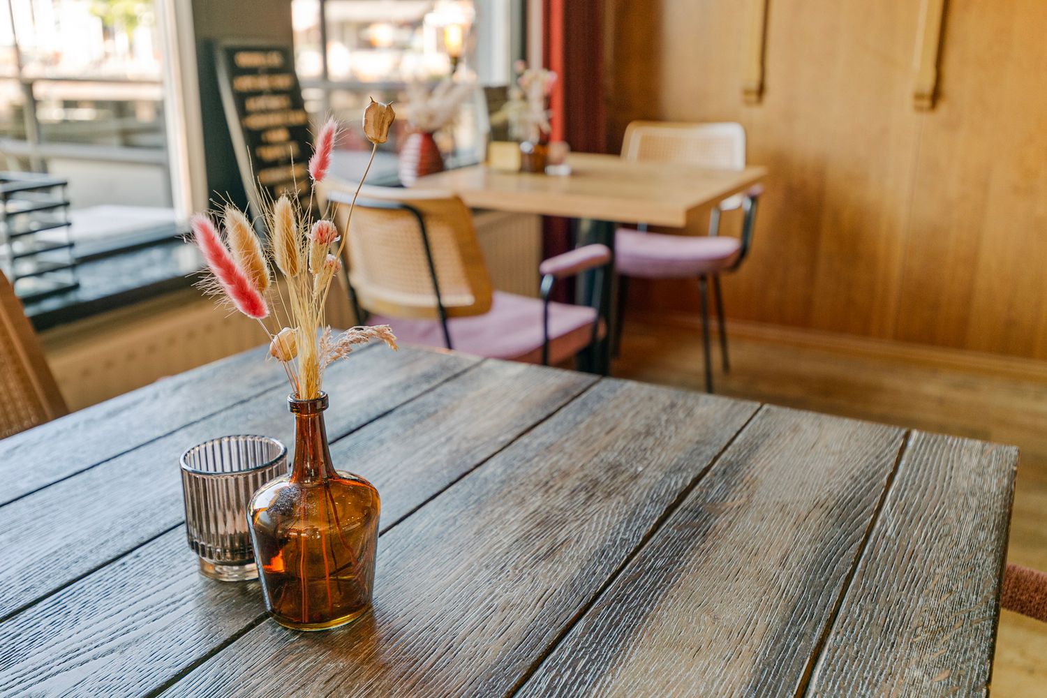 Rustic wooden table with amber glass vase and dried flowers in restaurant setting.