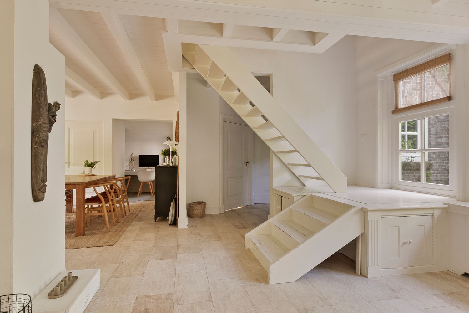 Modern white staircase with wooden steps and exposed beams in an open concept living space.