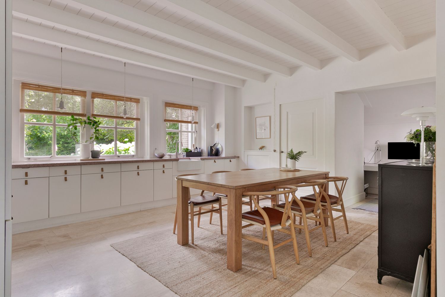 Bright open concept kitchen and dining area with white cabinets and wooden furniture.