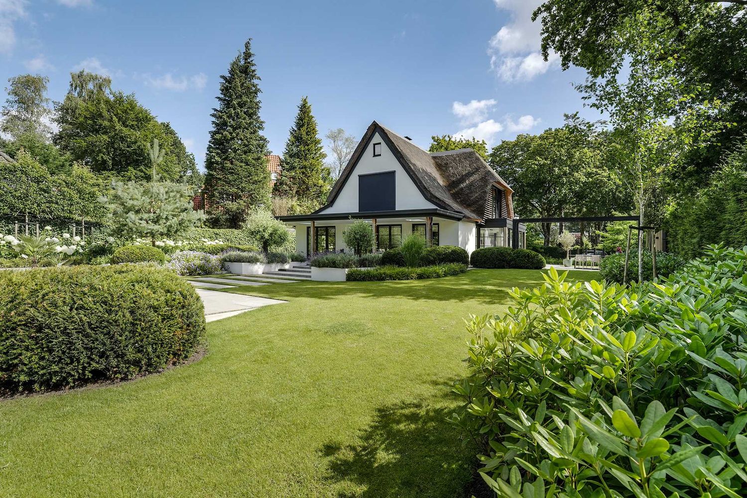 Expansive green lawn with trees and hedges surrounding a white residential property on a sunny summer day.