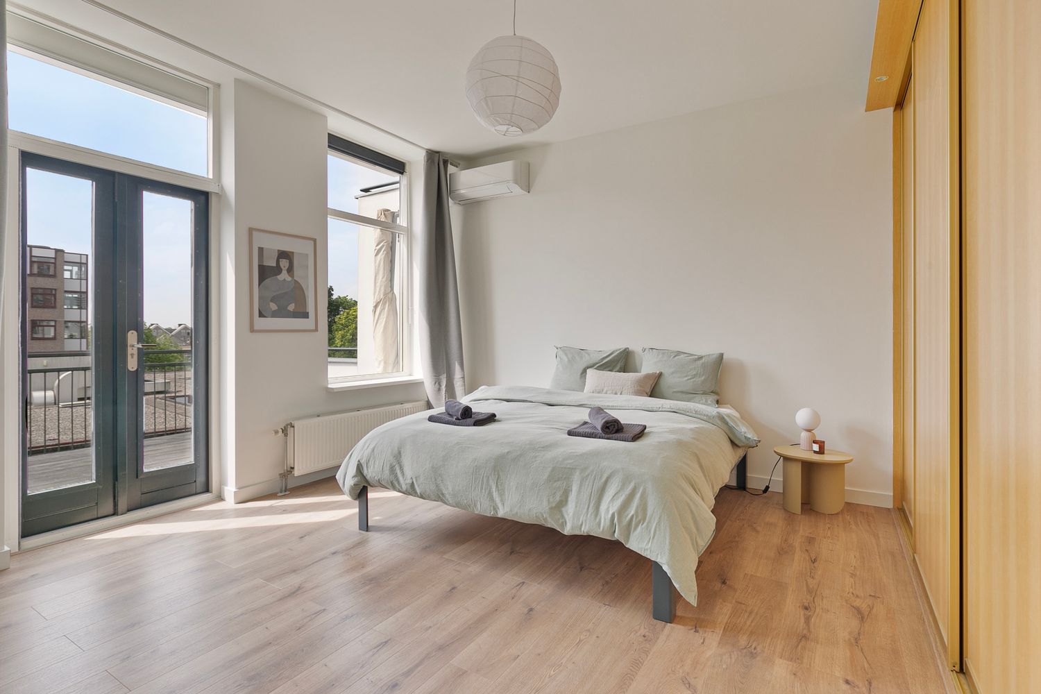 Serene bedroom with glass doors leading to balcony, featuring gray bedding and natural wood flooring.
