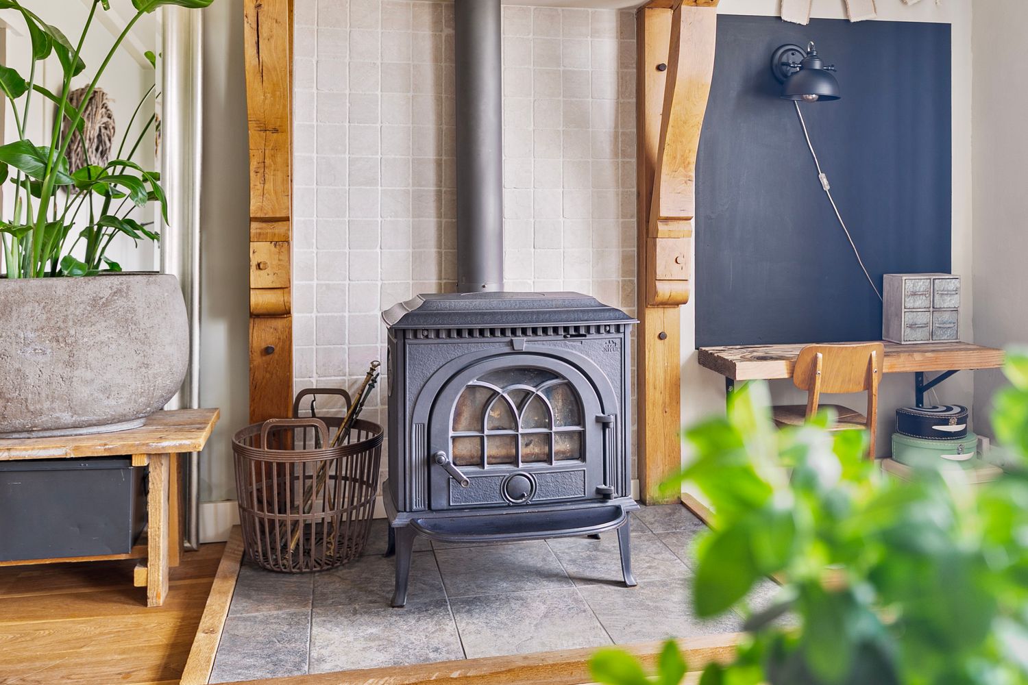Cast iron wood stove with decorative arch design sits beside potted plants in a cozy corner.