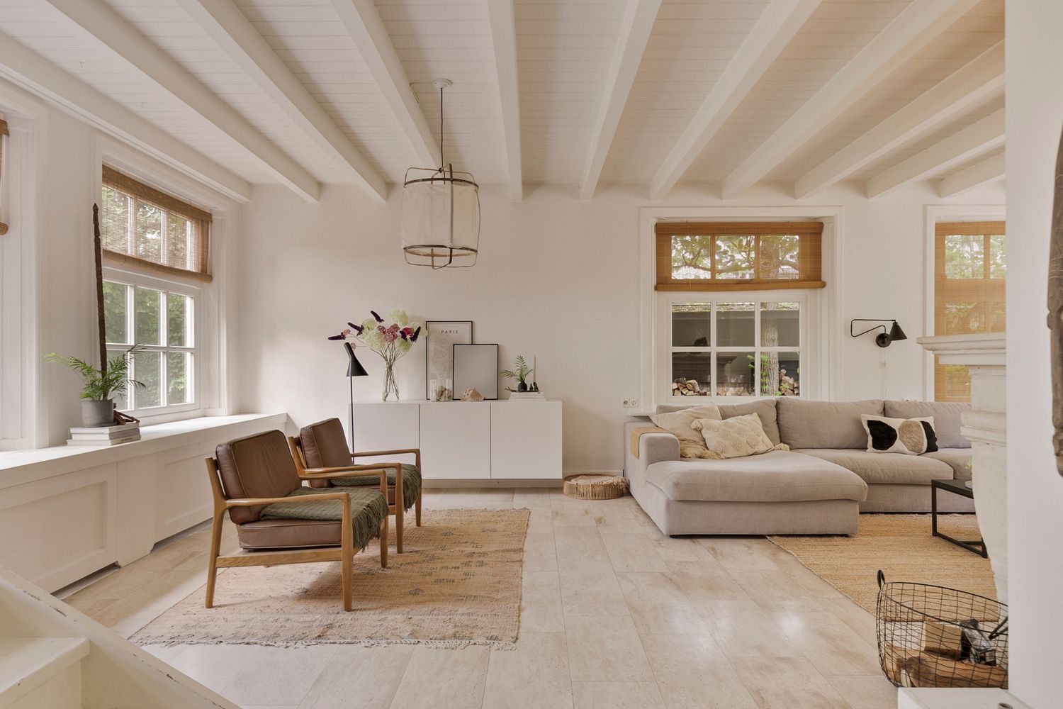 Minimalist living room with white walls, beamed ceiling, and comfortable neutral furniture.