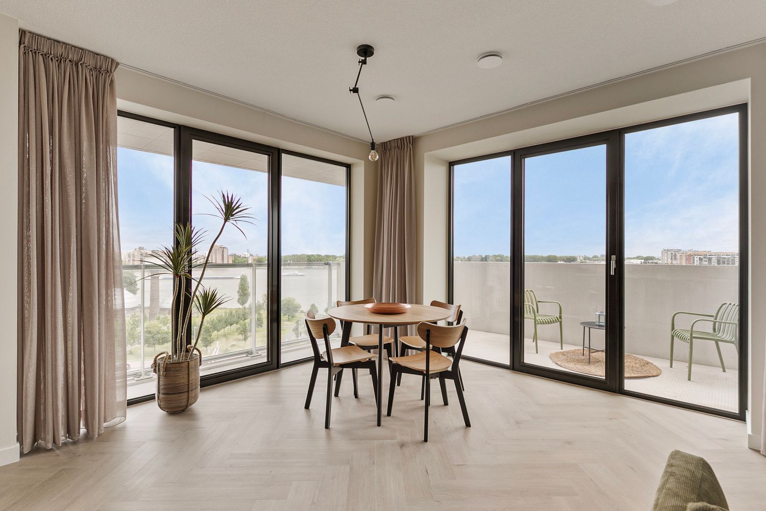 Bright dining space with floor-to-ceiling windows, round table, and wooden chairs in a modern apartment.