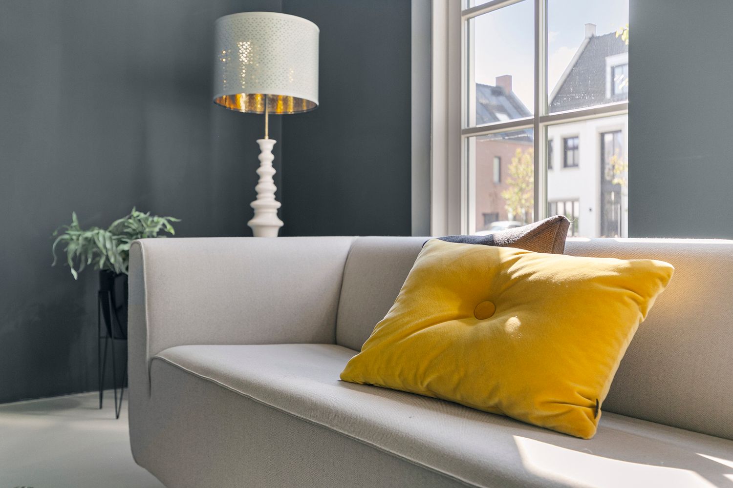 Modern gray sofa with gold accent pillow and decorative table lamp against blue-gray wall.