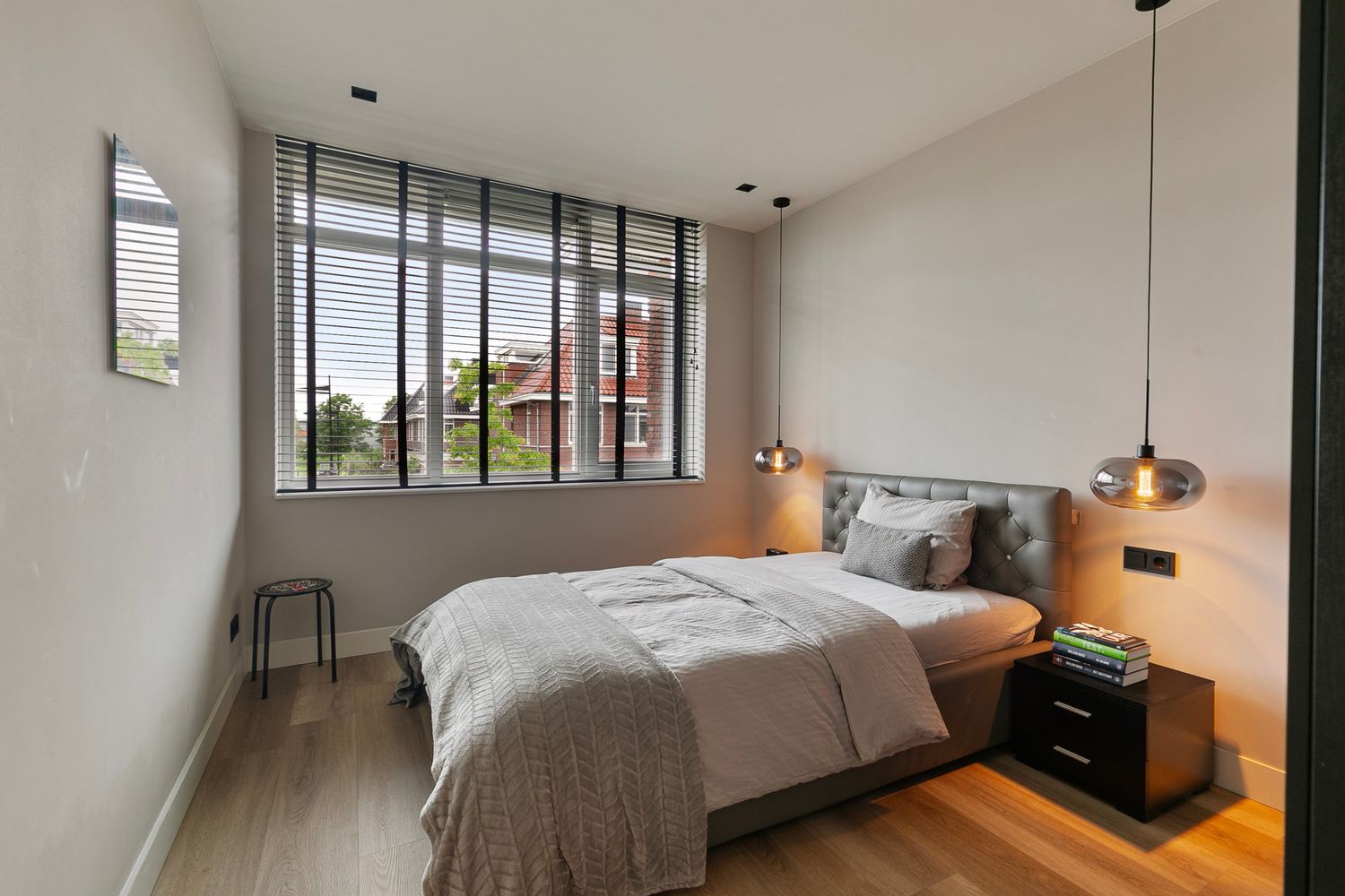 Minimalist bedroom with large windows, gray bedding, and pendant lights on either side.
