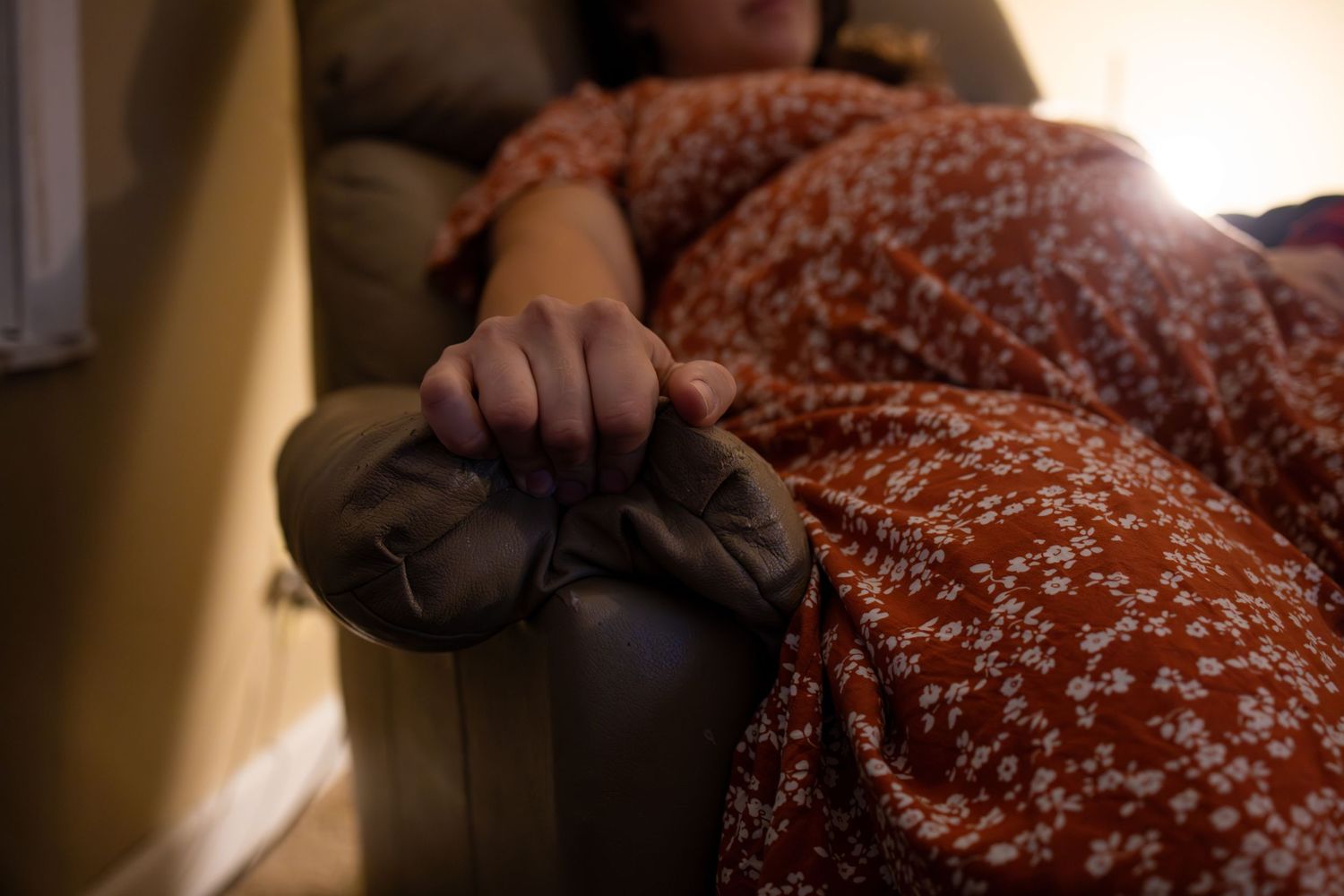 Close-up of hands resting on dark fabric against a floral pattern.