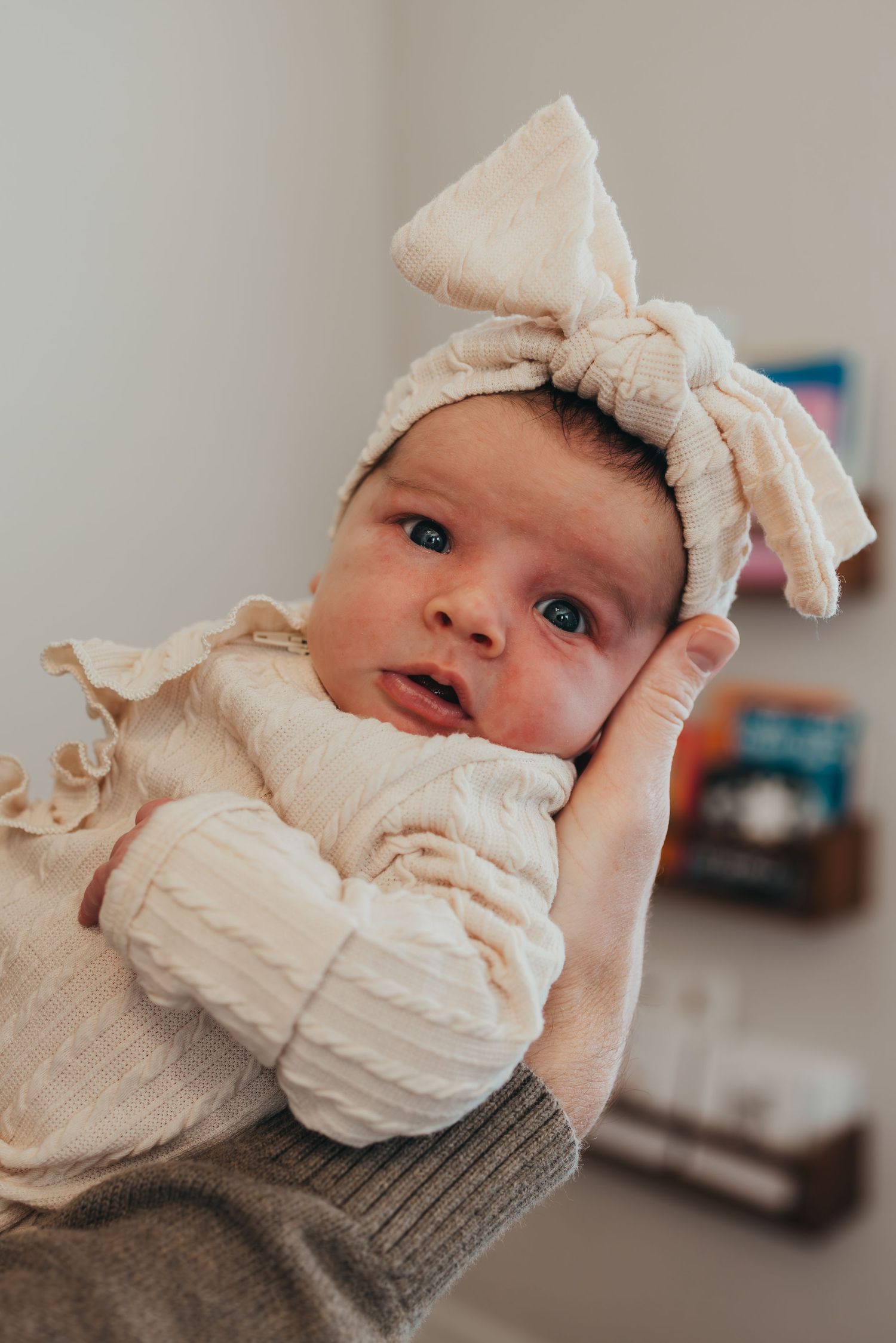 Baby wearing cream colored bow and ruffled outfit smiles while lying down.