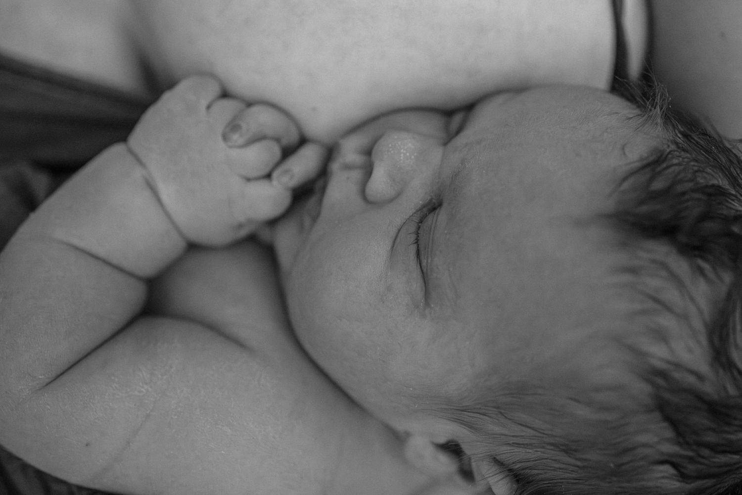 Close-up black and white portrait of a sleeping baby with tiny fists raised near their face.