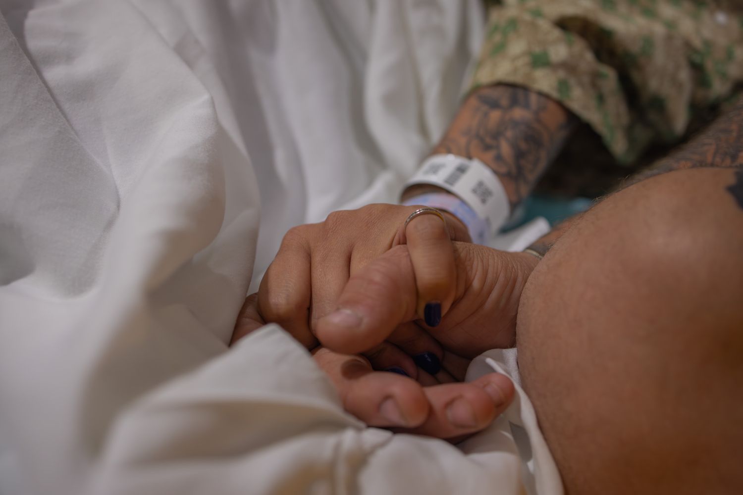 Close-up view of hands holding a newborn baby in a hospital bed.