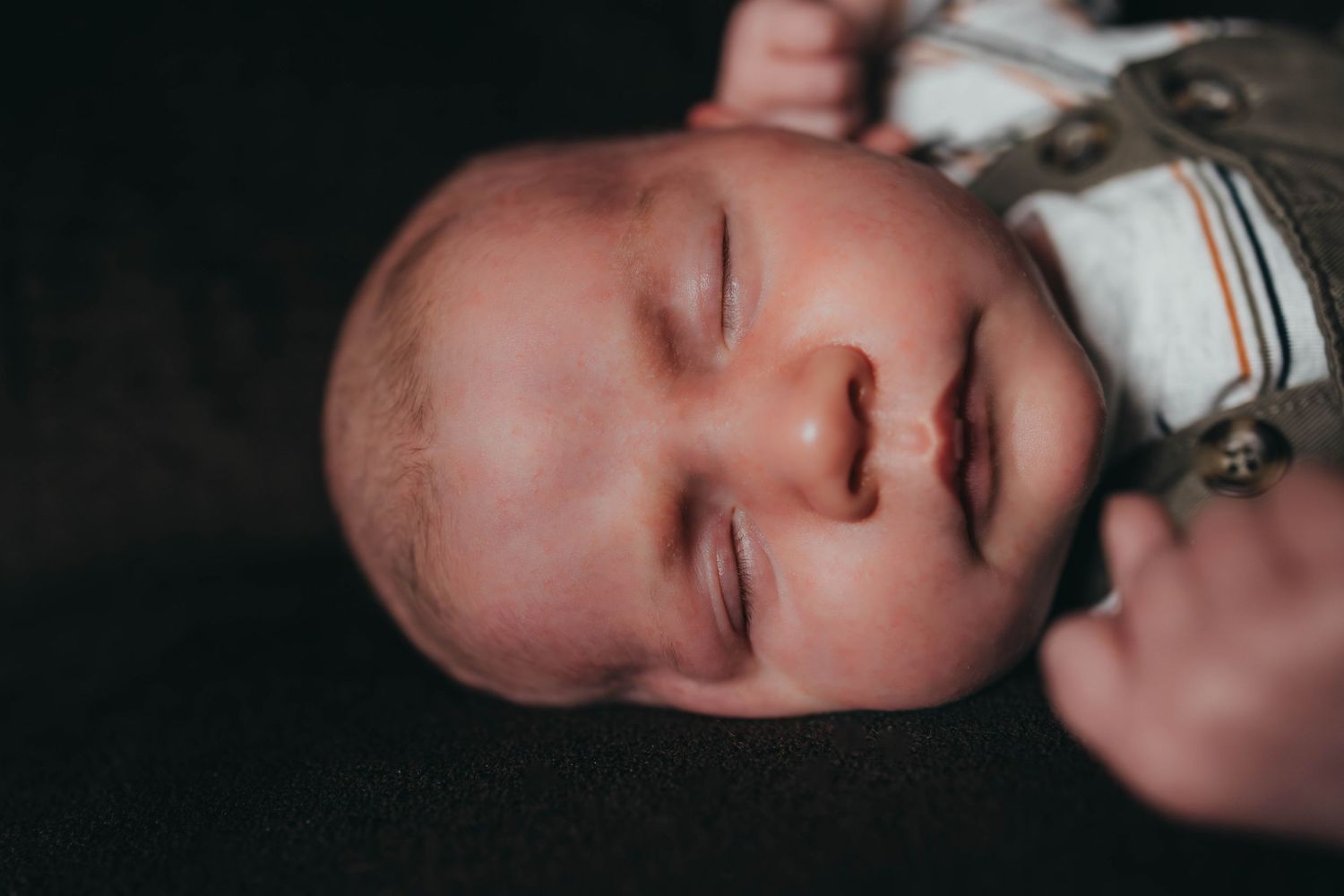 Close-up profile view of sleeping newborn in dark lighting.